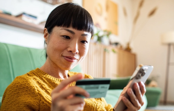 Frau mit Kreditkarte in der einen und Handy in der anderen Hand